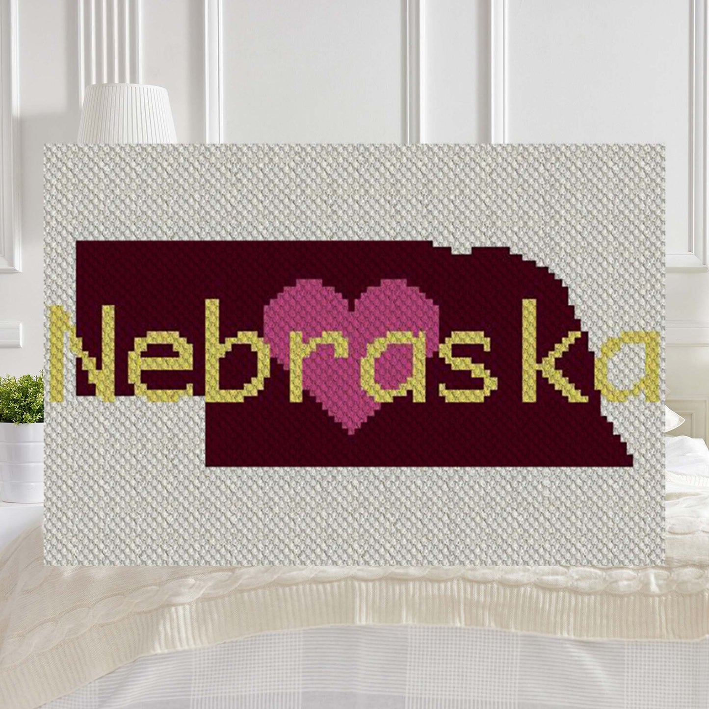 Pixel-art Nebraska outline with a heart in four contrasting yarn blocks