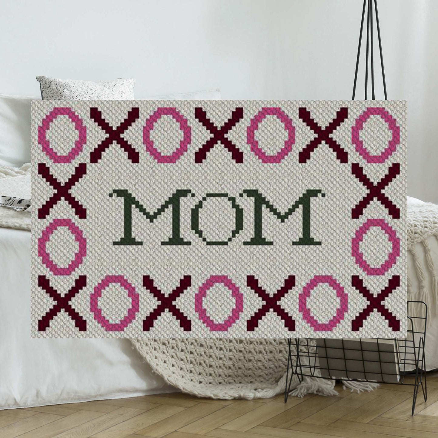 Pixel-art XOXO border in pink & burgundy around MOM†in dark green yarn blocks