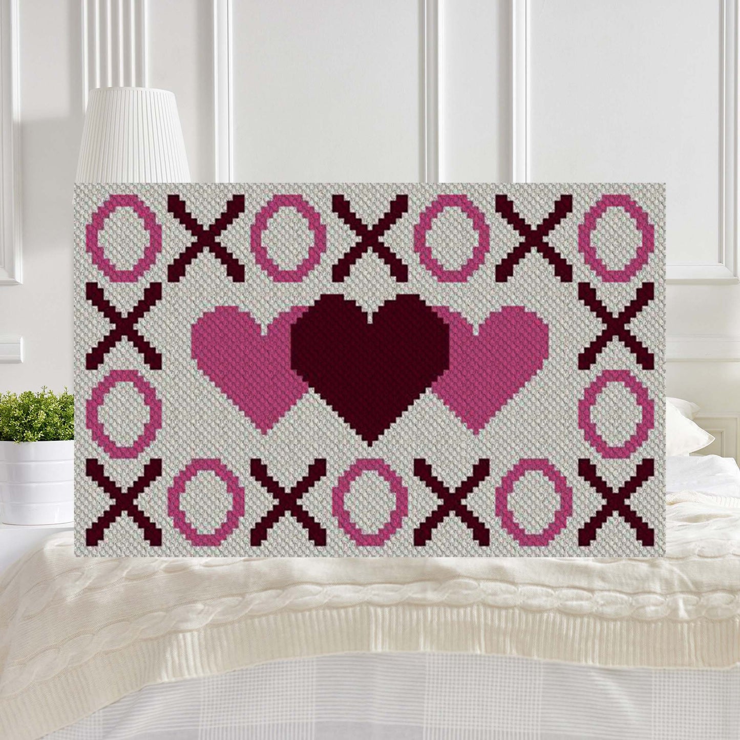 Pixel-art grid of X's, O's and hearts in pink, burgundy and gray yarn blocks